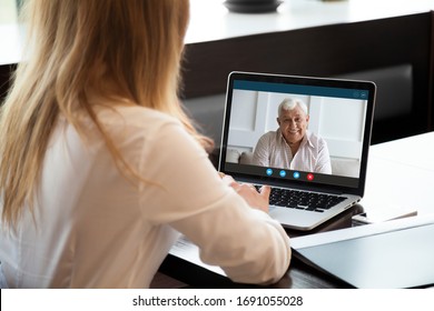 Back view of young woman sit on desk talk on video call with smiling elderly father, millennial female daughter have pleasant online webcam conversation on laptop with happy mature dad at home - Shutterstock ID 1691055028