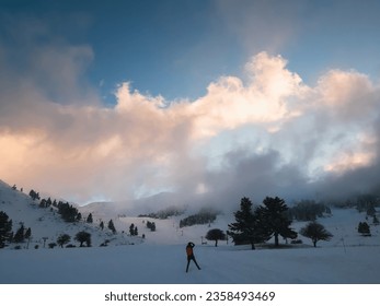 Back view of young woman standing at snowy slope and photographing the winter calm cloudy mountain landscape at sunset. Splendid snow-covered mountains view with beautiful fir trees on slope - Powered by Shutterstock