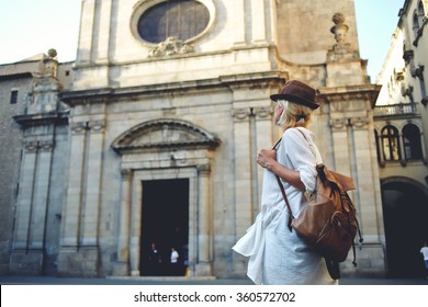 Back view of a young woman traveler with a backpack on her shoulder out sightseeing in a foreign city, stylish female foreigner examines architectural monument during her long-awaited summer vacation - Powered by Shutterstock