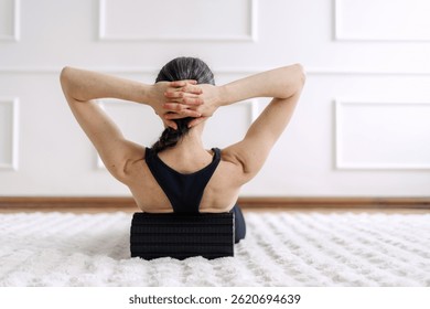 Vista posterior de la mujer joven utiliza un rodillo de espuma en su sala de estar para aliviar la tensión muscular después de hacer ejercicio. Reducir el dolor de espalda con fisioterapia, Autorización miofascial