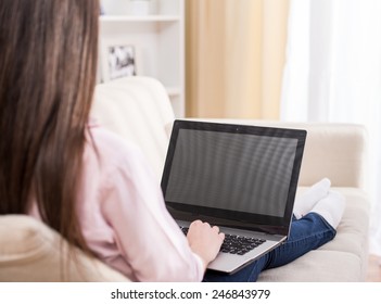 Back View Of Young Woman Is Using Laptop While Sitting On Couch At Home.