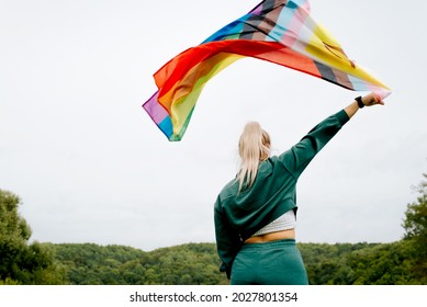 Back view of young woman waving rainbow flag against sky outdoors, new symbol of LGBTQ + community, rights and freedoms of gay lesbians traperson and people of different skin colors. Diversity concept