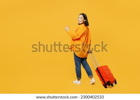 Back view young woman wear summer clothes walk go with suitcase bag show thumb up isolated on plain yellow background. Tourist travel abroad in free time rest getaway. Air flight trip journey concept
