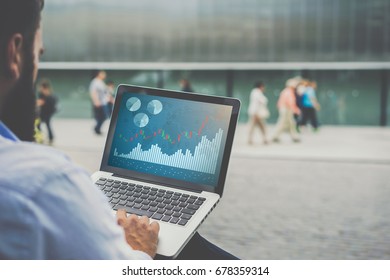 Back view.Close-up laptop with graphs, diagrams and charts on screen in hands of businessman sitting outdoors and working.Stock broker analyzes binary options charts.Student learning online. Marketing