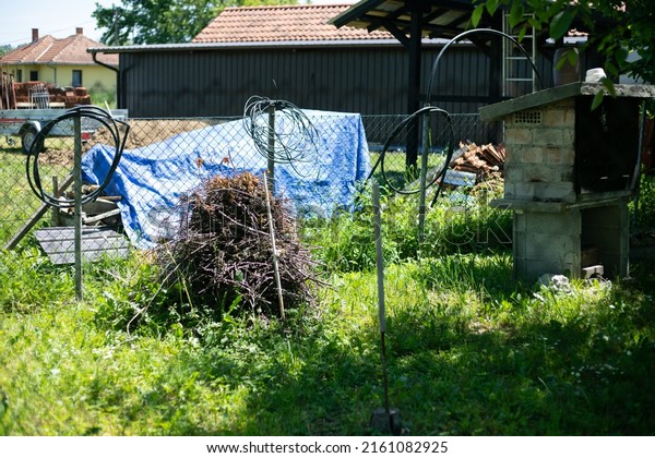 The back of\
the village yard. Wire fence, various cables hung. A brick\
barbecue, firewood, excess roof tiles, something covered with a\
blue tarpaulin and a neighbor\'s car\
trailer.