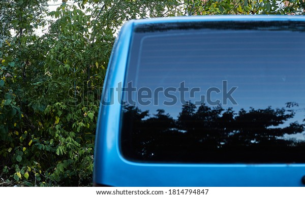 Back window of blue\
car parked on the street in summer sunny day, rear view. Mock-up\
for sticker or decals
