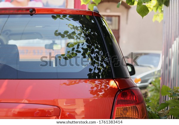 Back window of red\
car parked on the street in summer sunny day, rear view. Mock-up\
for sticker or decals