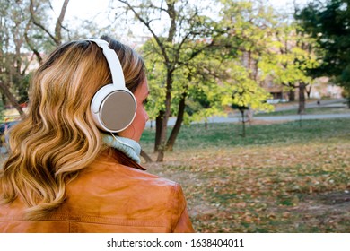 Back Of Woman Head With Big White Earphones Looking Autumn Tree.Close Up  Hair And Music Headphones