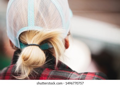 The Back Of A Woman Head Wearing A Messy Ponytail Under Her Hat
