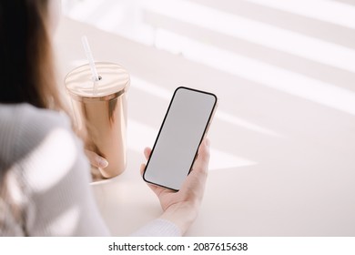 The Back Of A Woman Holding A Tumbler And A Cell Phone.