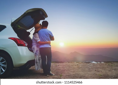 Back of woman hugging man and looking mountain view in sunrise. Couple travel at mountain in holiday by hatchback car. Love