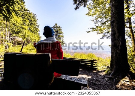 Back woman person sitting on wooden bench looking at high angle overlook of autumn fall red maple landscape leaf color trees in Gaudineer knob Monongahela national forest Shavers Allegheny mountains