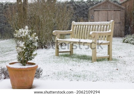Back yard (backyard) covered in snow in winter, with a teak hardwood wooden bench on lawn. England, UK