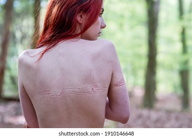 Back of young beautiful sexy woman with long red hair in forest with imprints of tied rope from bondage on bare skin