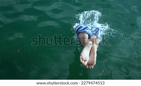 Back of young boy diving into water. Active child splashes inside lake. Kid enjoying summer vacations