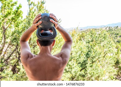 Back Of Young Fit Shirtless Man With Heavy Kettlebell Doing Triceps Exercise And Muscles In Outdoors Outside Park Holding Weight Lifting