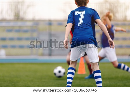 Back of young soccer boy playing game on grass school field. Young football player in blue jersey sports shirt with number seven on his back