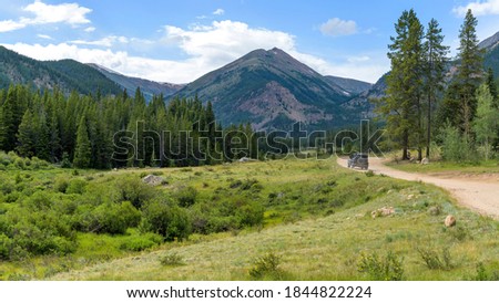 Backcountry Road - A remote Forest-Service-Road winding in a green valley towards high peaks of Continental Divide on a sunny Summer evening, near Guanella Pass, Grant, Colorado, USA.