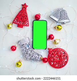 Backdrop Of Christmas Decorations On A White Background With Lights And In The Center A Smartphone With A Green Screen