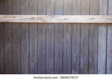 Backdrop or rustic background of dark stained fence featuring a sturdy horizontal wooden beam across its upper section and vertical panels   