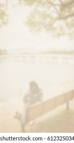 Background abstract blurred of Woman sitting at a lakeside bench under a large tree. , Feeling lonely
