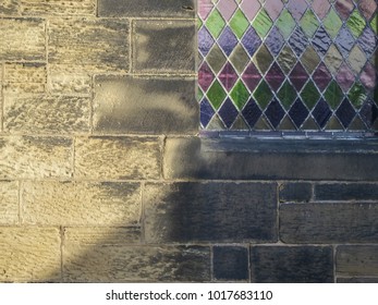 Background abstract detail of an old sandstone church wall and stained glass window in part shadow on a sunny day.