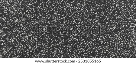Background of an asphalt pavement surface with a granular texture, featuring embedded fragments of white stone in a dark base