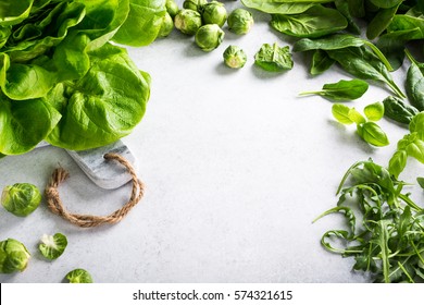 Background with assorted green vegetables, fresh lettuce salad, spinach, rucola, Brussels sprouts and basil on light gray stone table. Healthy food concept with copy space.