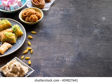 Background with assorted traditional eastern desserts. Different Arabian sweets on wooden table. Baklava, halva, rahat lokum, sherbet, nuts, dates, raisins, kadayif in colorful plates. Selective focus