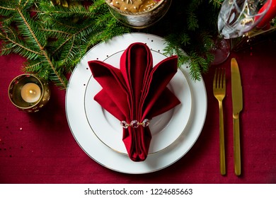 Background Of Beautiful Served Table With Candles, Red Tablecloth And Napkins, White China, Gold Cutlery, Crystal Champagne Glasses, Spruce Tree Branches. Top View. Holiday Setting, Christmas Mood.