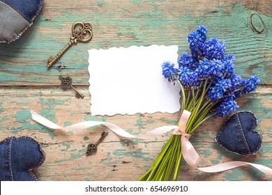 Background with blank paper card, bouquet of blue flowers, denim hearts and vintage keys on old wooden boards. Place for text. Top view. 