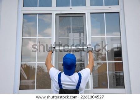 Background of blue-cap worker installing a mosquito net on large plastic window outside the building in summer. Professional installation of an additional insect net on window