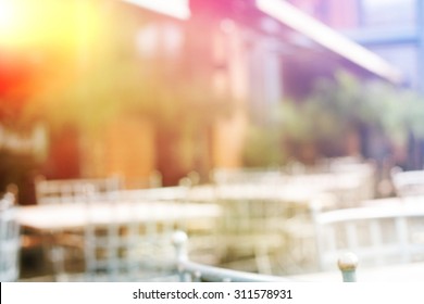 Background Of Blurred Cafe On Street Of City. Tables And Chairs Outside In Natural Bokeh