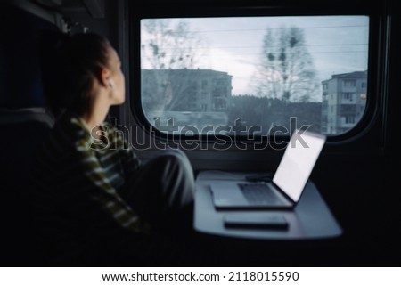 Background. Blurred photo of female tourist with laptop on table traveling by train. Focus on the gray city outside the window.
