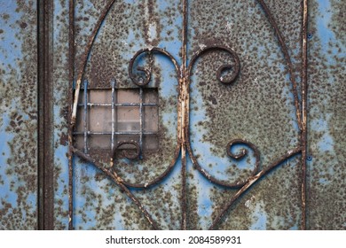 Background Detail of a blue rusty iron door with wrought iron ornament and small dirty window reflecting a modern window