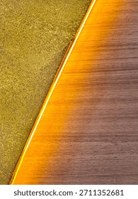 Background of a diagonal geometric pattern with two distinct textures for decoration. Interior decor combines handcrafted gold glitter and walnut wood separated by a diagonal strip of yellow lighting.