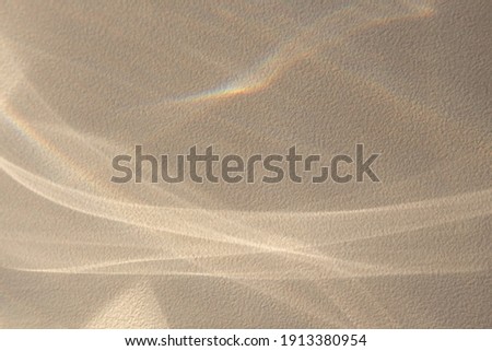Background with the effect of reflection of abstract shiny lines with natural shadows and rays of light from a window on a textured wall in a delicate sandy color. Copyspace for mockup and posters.