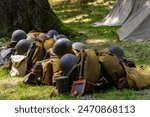 Background. Equipment of Polish infantry soldiers during the Polish defensive war of 1939.  A pile of backpacks, helmets and other equipment in the woods.