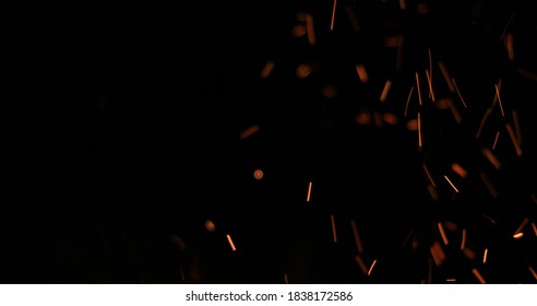 Background of feint blurred orange sparks from fire against black with copyspace