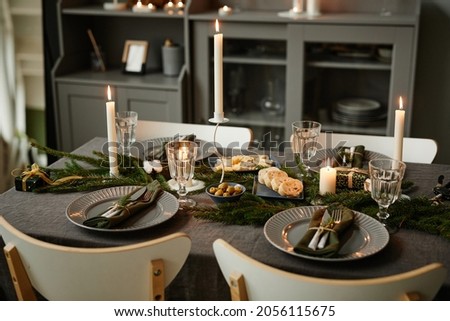 Background image of cozy table setting decorated for Christmas with candles lit in grey tones, copy space