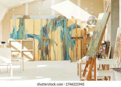 Background Image Of Empty Art Studio In Attic Lit By Sunlight, Focus On Easel And Abstract Paintings, Copy Space