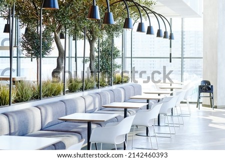 Background image of empty food court interior in shopping mall with tables and chairs in neutral grey tones lit by sunlight, copy space