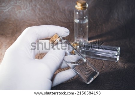 Background image with focus on a laboratory flask and a gloved hand filled with a clear solution on a brown background. High quality photo