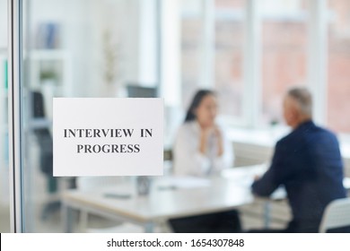 Background Image Of Job Interview In Progress Sign On Glass Door In Modern Office With Blurred Silhouettes Of Two People Talking, Copy Space