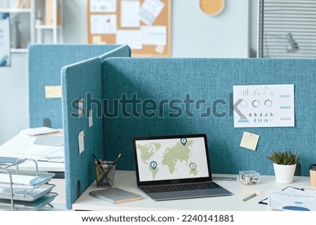 Background image of office cubicle with laptop on desk and world map graphs, copy space