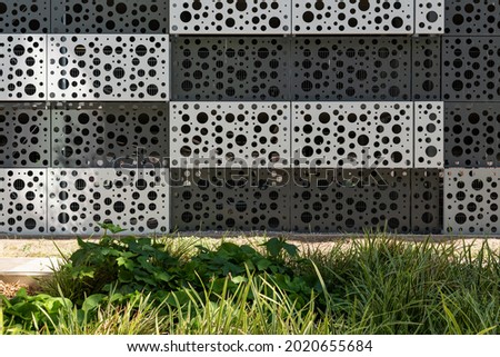 Background image of a perforated facade with a green foreground