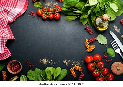 Background. Italian Food. Multicolored Pasta, Tomatoes, Spinach, Basil Leaves And Olive Oil On A Dark Surface. Place For Text In The Center.