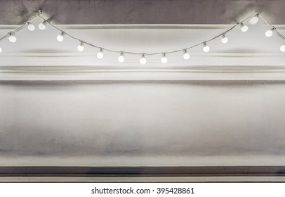 Background Of Light Bulbs String Decorated On A White Wall At Night.