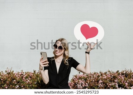 The background is a light gray brick wall, providing a smooth, minimalist background. Gray color complements the scene's simplicity. Woman on social media holding a heart in speech bubble, background.