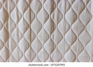 Background of the light gray quilted fabric of an old slightly deformed mattress with side lighting